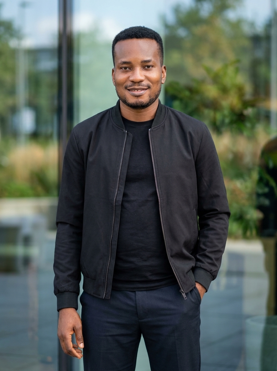 Amb. John Ifeanyi Amos in black bomber jacket reflecting musical artistry as AMOS JOHN